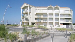 Un immeuble résidentiel à plusieurs étages, doté de balcons, d’un espace de stationnement et d’un chemin piétonnier.
