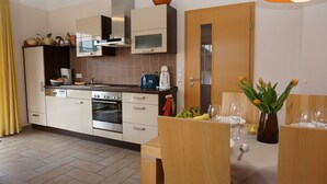 Una cocina moderna con horno empotrado, microondas y estufa. Hay un comedor con una mesa de madera preparada para dos personas, y un florero con flores sobre la mesa.