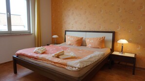 Una cama impecablemente arreglada con una colcha estampada y dos almohadas, flanqueada por dos mesitas de noche con lámparas, en una habitación con papel tapiz decorado y una ventana con cortinas.