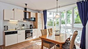A modern kitchen with white cabinets, a dining table with wicker chairs, and large windows with blue curtains. - Villa beach pearl, Apt. 19 - Villa beach pearl, apt 19. (Heringsdorf)