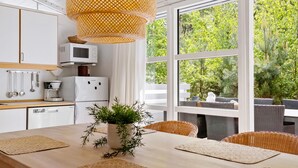 Une cuisine moderne avec des meubles blancs, un four à micro-ondes et une machine à café. On y trouve une table à manger avec des sets de table en fibres naturelles et une plante en pot.