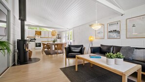 Un salon moderne avec une cheminée, un canapé, un coin repas et une cuisine visible à travers une porte ouverte.
