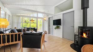 Un salon moderne avec un poêle à bois noir, un canapé, une table à manger et un téléviseur fixé au mur.