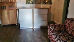 A room with a wooden cabinet, a white dresser, a patterned sofa, and a wall-mounted artwork. - 6 - "Up'n Hoff", Germany (Middelhagen)
