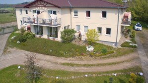A two-story building with a balcony, a driveway, and a garden with various plants and flowers.