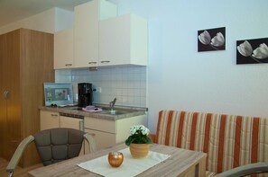A compact kitchen with white cabinets, a microwave, and a coffee maker. There is a dining table with a vase and a chair. A striped sofa is against the wall.