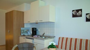 A compact kitchen with a microwave, coffee maker, and a sink. There is a dining table with a chair and a striped sofa.