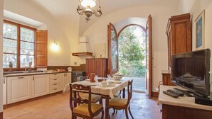 A kitchen with wooden cabinets, a dining table set for four, and a television on a stand. - Lovely apartment in Rosignano LI (Rosignano LI)