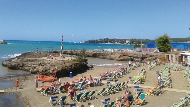 A beach with rows of beach chairs and umbrellas, rocky outcrops, and a clear view of the sea. - Lovely apartment in Rosignano LI (Rosignano LI)