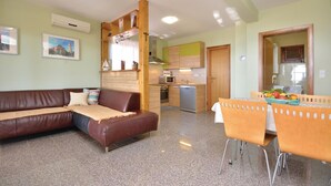 Ein Wohnzimmer mit braunem Ledersofa, einem Esstisch mit orangefarbenen Stühlen und einer Küchenzeile mit Mikrowelle und Backofen.