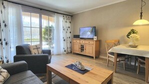Ett vardagsrum med en soffa, ett soffbord i trä, en tv-apparat placerad på ett skåp och ett matbord med stolar.