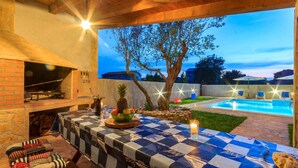 Un patio al aire libre con una parrilla, una piscina y un mantel a cuadros.