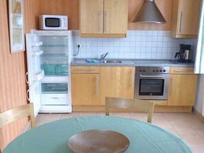 A kitchen with wooden cabinets, a microwave, a refrigerator, an oven, and a dining table with a green tablecloth.