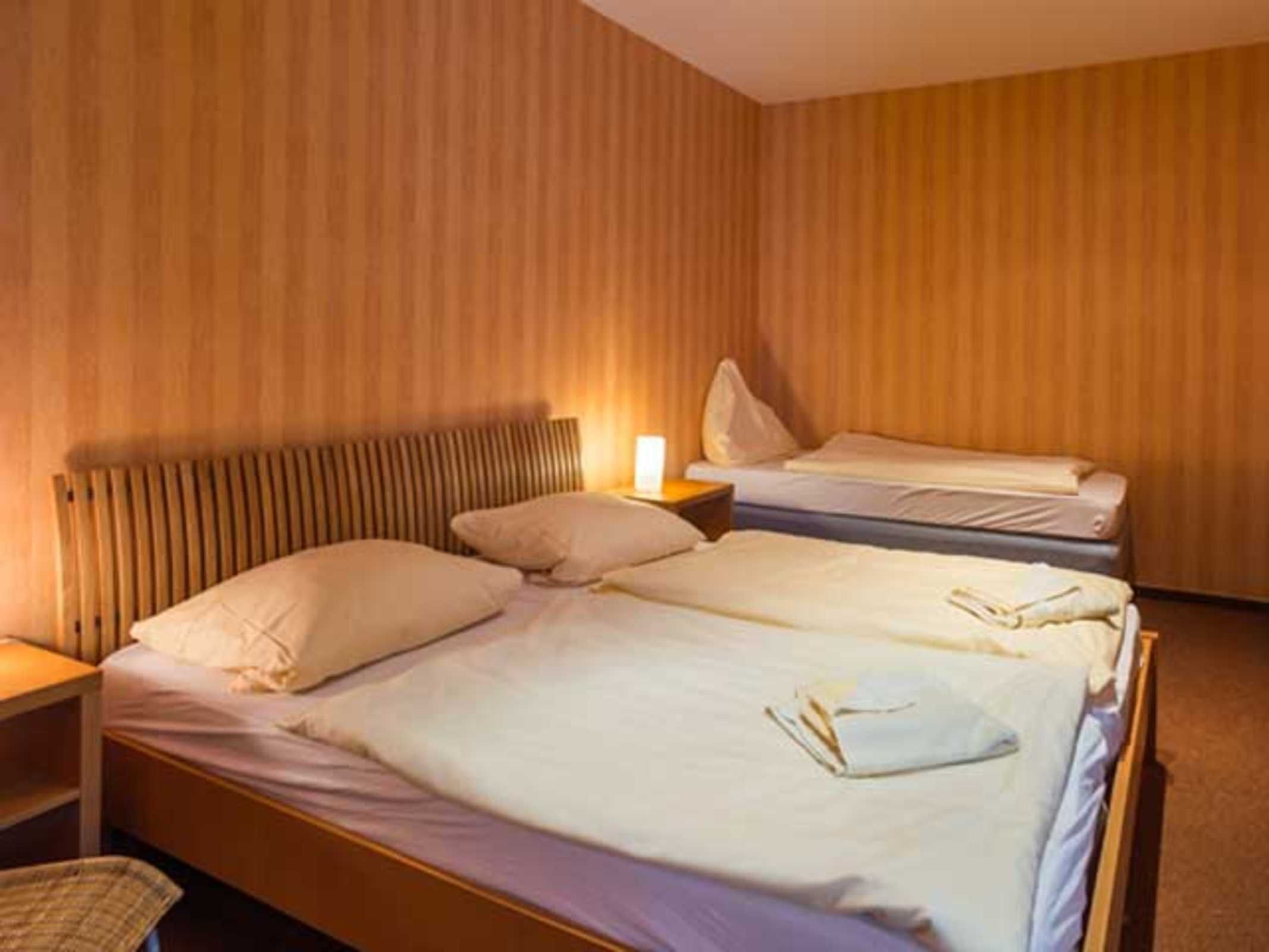 Ein Hotelzimmer mit zwei Betten, einem hölzernen Kopfteil, einem Nachttisch mit Lampe und einem Sessel.