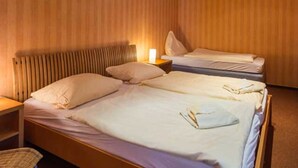 Habitación de hotel con dos camas, cabecero de madera, mesita de noche con lámpara y una silla.
