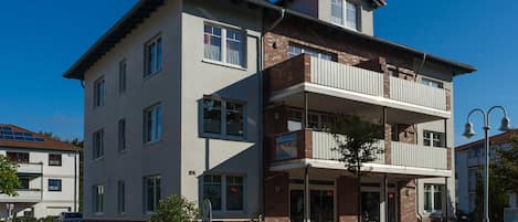 A multi-story building with a balcony, a bicycle parked outside, and a clear blue sky.