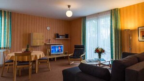 Una sala de estar con un sofá, un televisor, una mesa de comedor con sillas y un reloj en la pared.