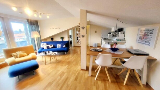 A modern living room with a blue sofa, a yellow armchair, and a wooden dining table with white chairs. - (207) 2-room apartment - Appartementhaus Strandstr. 16 (Kühlungsborn)