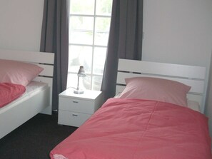 A twin room with two beds, each with a pillow and a bedside table with a lamp.