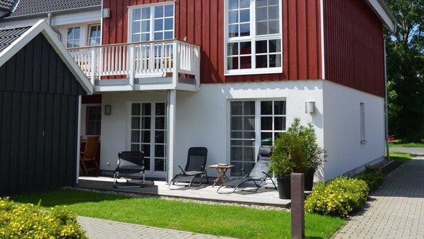Ein zweistöckiges Haus mit roter Fassade, weißem Zierdekor und einem Balkon mit weißer Geländer.