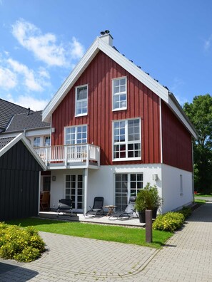 Ein zweistöckiges Haus mit roter Fassade, weißem Zierdekor und einem Balkon mit weißer Geländer.