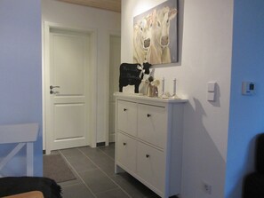 A hallway with a white door, a white cabinet with drawers, and a painting of cows on the wall.