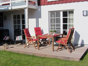 Eine Terrasse mit einem Holztisch und vier roten Stühlen, einem kleinen Hocker und einer Bank.