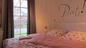Ein Schlafzimmer mit Bett, Fenster mit Vorhängen, einer Wand mit einem Schild und einem Heizkörper.