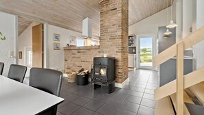 A modern kitchen with a brick fireplace, a dining area with chairs, and a view through a glass door. - Amazing home in Hvide Sande with sauna (Hvide Sande)
