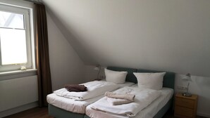 A twin bed with two pillows, a bedside table with a lamp, and a window with curtains. - Double room 05 (H) - guest house & beach hall (Ahrenshoop)