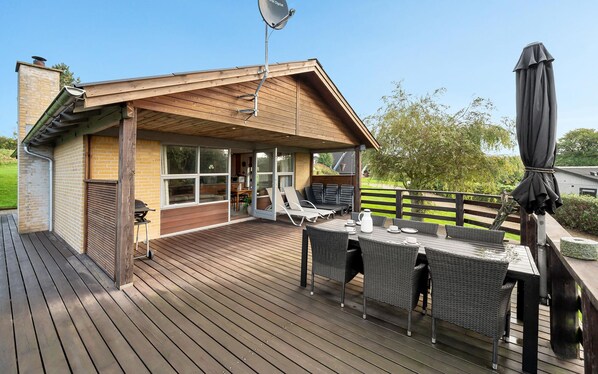 En træterrasse med udendørs møbler og en overdækket patio.