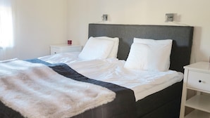 A neatly made bed with white bedding and a dark headboard, accompanied by a white nightstand and a small bedside table with a red object on it. - Awesome home in Sälen with sauna (Sälen)