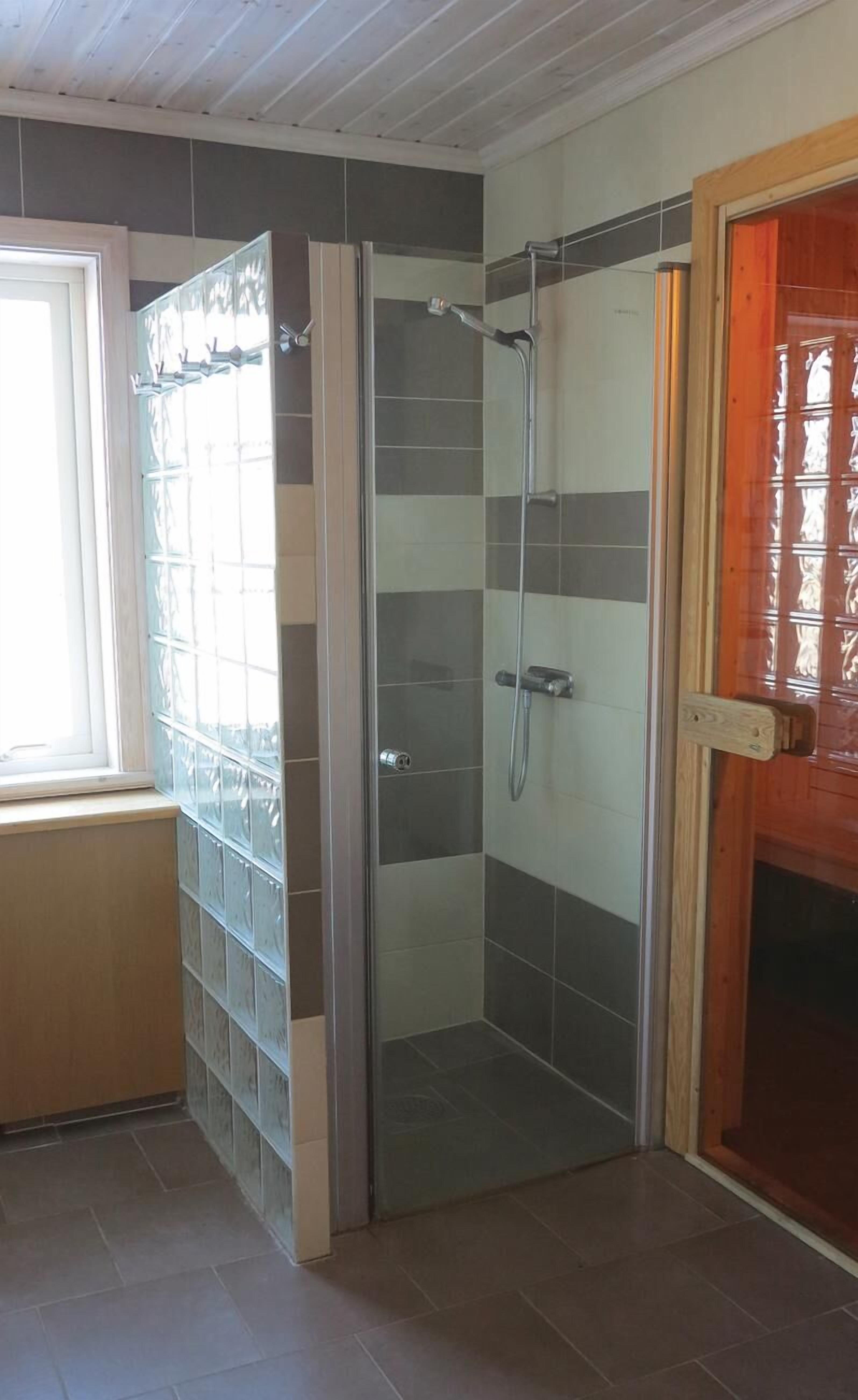 Un espace douche doté d’une porte en verre, de murs carrelés et d’un cadre de porte en bois.