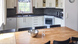 A modern kitchen with white cabinets, a black backsplash, and a wooden dining table with chairs. - Awesome home in Sälen with sauna (Sälen)
