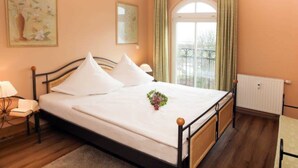 A bedroom with a bed, a nightstand, a lamp, a window with curtains, and a radiator. - (21) 3-room apartment - lake view - apartment house Atlantik (Kühlungsborn)