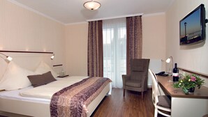A hotel room with a bed, a desk with a chair, a TV, and a window with curtains.