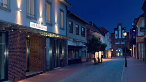 A hotel with a sign reading "HOTEL HOLLANDERSROOD" on a brick facade, a cobblestone street, and a few people sitting on benches.