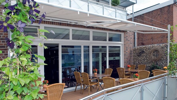 An outdoor patio with wicker furniture, a glass railing, and a brick wall in the background.