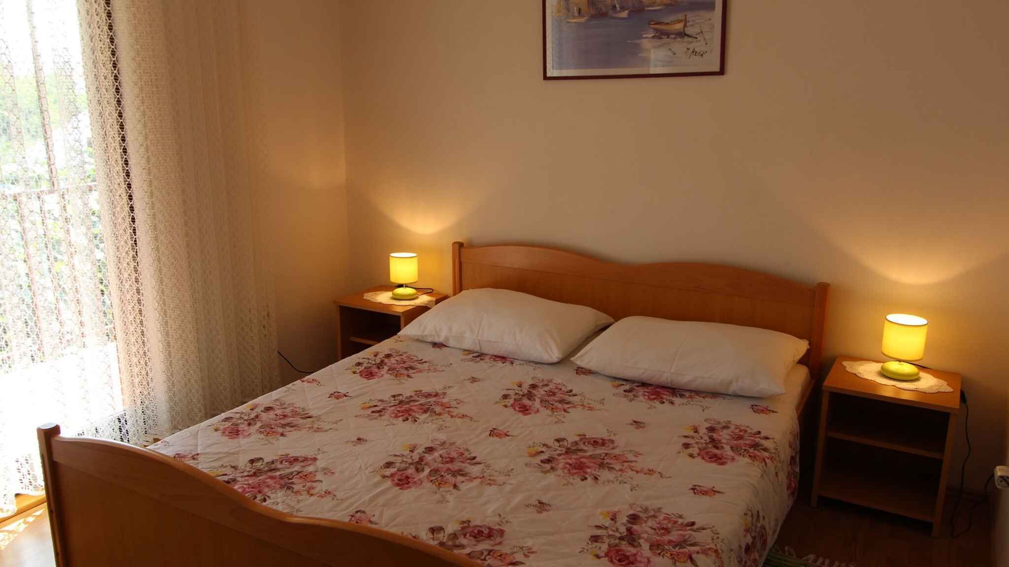 A bedroom with a wooden bed, floral bedding, two bedside lamps, and a painting on the wall.