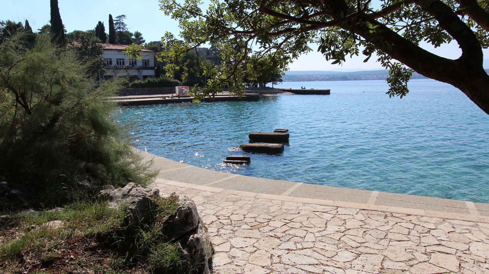 Un sendero de piedra que conduce a una masa de agua tranquila con un muelle y un edificio al fondo.