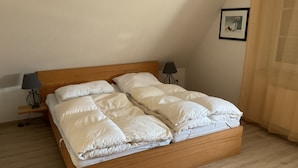 A neatly made bed with a wooden frame and white bedding, two bedside lamps, and a framed picture on the wall. - Vacation home in Nessmersiel 20-040a - 200-040a (Dornum)