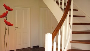 A staircase with wooden steps and white balusters, leading to a room with dark tiled flooring and white doors. - Vacation home in Nessmersiel 20-040a - 200-040a (Dornum)