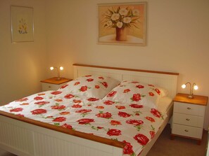 Ein ordentlich bezogenes Bett mit Blumenmuster, zwei Nachttische mit Lampen und ein gerahmtes Bild mit floralem Dekor darüber.