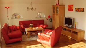 A living room with red sofas, a wooden cabinet, a TV, and artwork on the wall. - Vacation home in Nessmersiel 20-040a - 200-040a (Dornum)