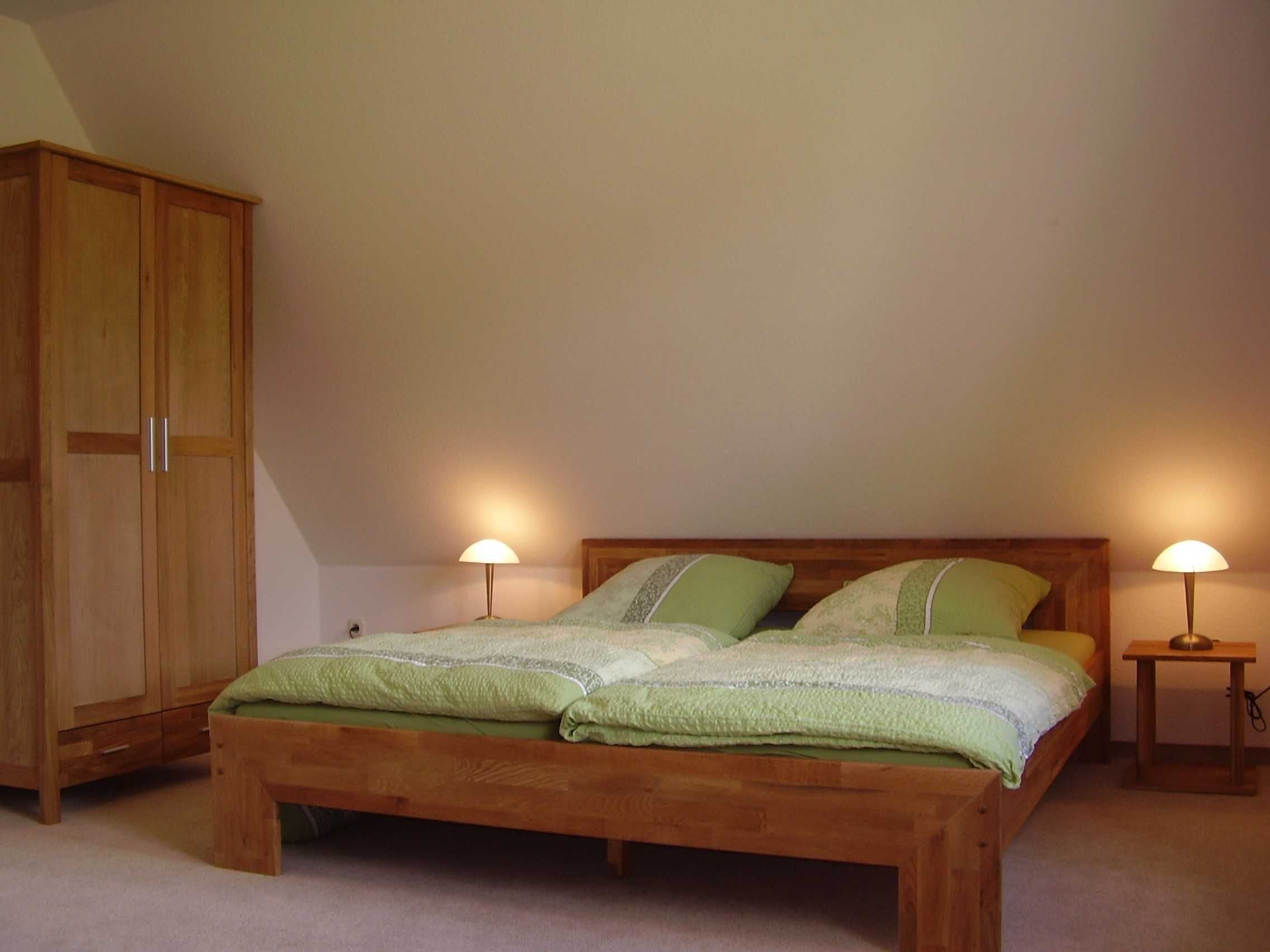 Un dormitorio con una cama de madera, dos lámparas de noche y un armario de madera.