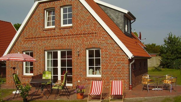 A brick house with a sloped roof, a patio with outdoor furniture, and a large umbrella. - Vacation home in Nessmersiel 20-040a - 200-040a (Dornum)
