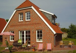 Ein Ziegelhaus mit geneigtem Dach, einer Terrasse und Gartenmöbeln sowie einem großen Sonnenschirm.