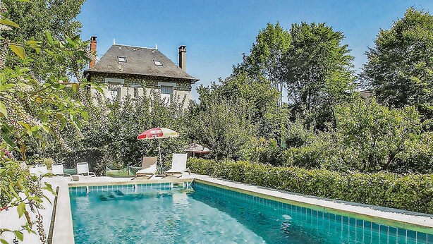 A swimming pool with lounge chairs and an umbrella, surrounded by lush greenery and a large house in the background.