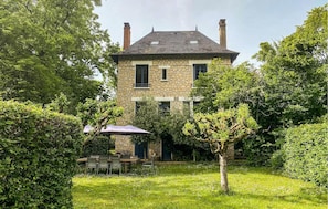 Une maison en pierre avec un jardin, un espace extérieur aménagé pour s’asseoir et une terrasse couverte.