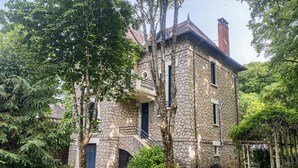 A stone building with a balcony, a chimney, and a small wheelbarrow.